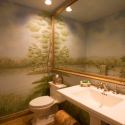 A bathroom with a mural and large mirror on the walls.